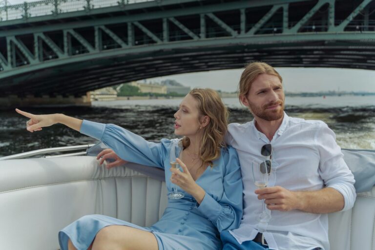 Couple enjoying a romantic boat ride under a bridge, sipping champagne.